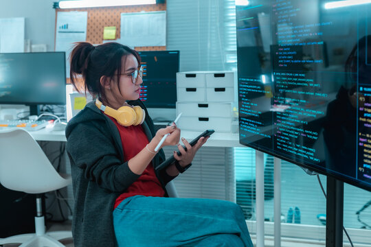 Software developer reviewing source code on large display using digital pen and smartphone in office, representing programming, software engineering, code analysis, digital workflow and technology.