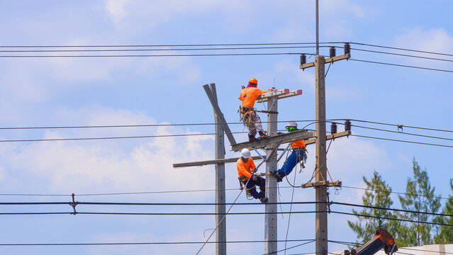 Electricians group working on concrete power pole to installing cables and electrical equipment against blue sky background