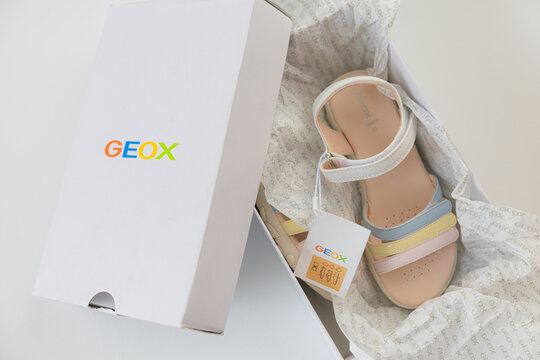 Unboxing new Geox girls sandals with multicolored pastel straps in branded white box over white background