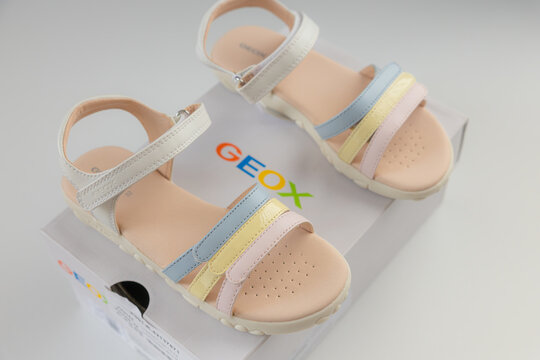 Unboxing new Geox girls sandals with multicolored pastel straps in branded white box over white background
