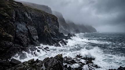 Obraz premium Dramatic coastal landscape featuring rugged cliffs and crashing waves under a moody sky with dark clouds and mist over the ocean in a remote area