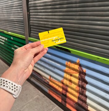 Passenger displays a Navegante card at Lisboa Oriente train station in a close-up view of a hand holding the public transport pass against a landmark mural and metal shutter, Lisbon, 2 April 2026