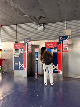 Passenger buys a ticket at Lisboa Oriente train station from a branded Fertagus self-service machine while carrying a large backpack beside a contactless fare validator, Lisbon, 2 April 2026