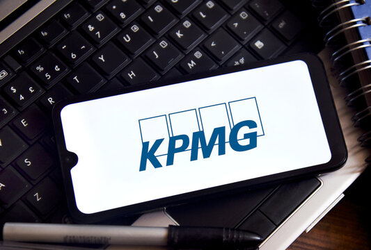 KPMG corporate logo displayed on a smartphone screen over a laptop keyboard with a pen, conceptual business and financial services illustration.