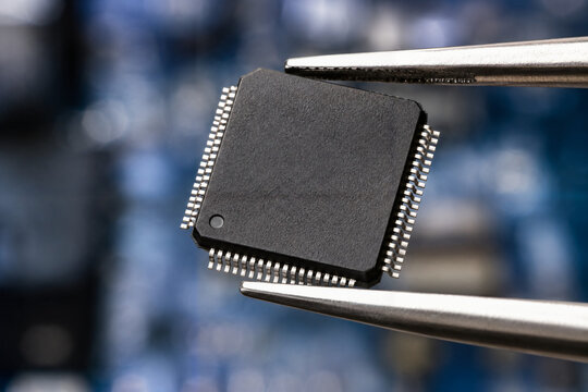 Macro close up of a black computer microchip held by metal tweezers