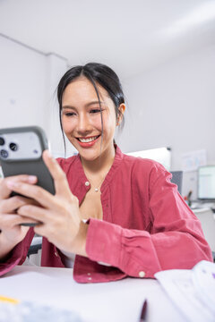 Young woman smartphone office smile, casual worker using mobile phone at desk with happy expression, modern indoor workplace, communication and technology Vertical