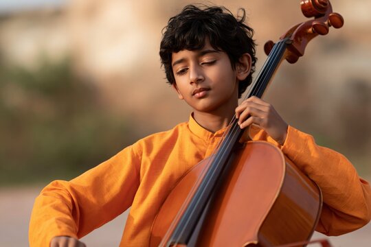 Young boy playing cello outdoor portrait in orange kurta for music education banner and background use
