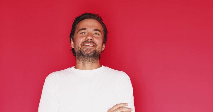 Happy cheerful middle aged Caucasian man laughing out loud with joyful facial expression and arms crossed looking at camera on vibrant red studio background portrait, authentic positive emotion video