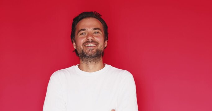 Handsome middle aged Caucasian man smiling happily and looking at camera with friendly facial expression then turning serious on vivid red studio background, positive portrait stock video