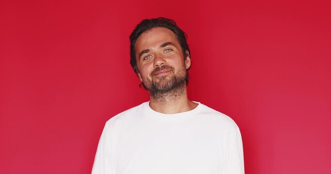 Handsome middle aged Caucasian man turning head from side profile, running hand through hair and smiling confidently looking at camera on red background, hair styling and grooming motion video clip