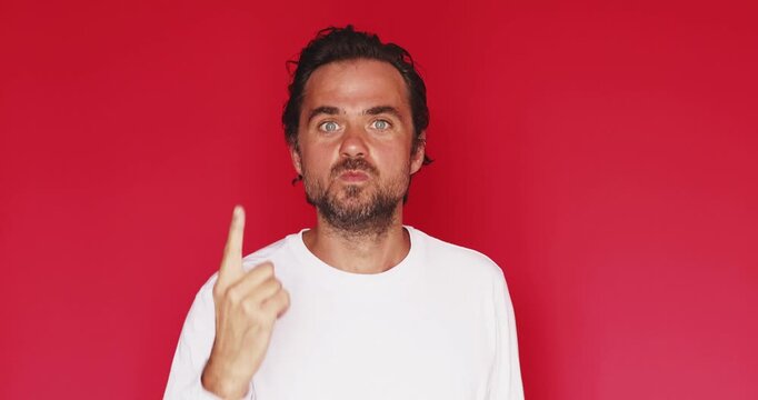 Handsome middle aged Caucasian man pointing index finger up giving advice or warning with expressive face then smiling on bright red studio background, attention tip attention concept clip