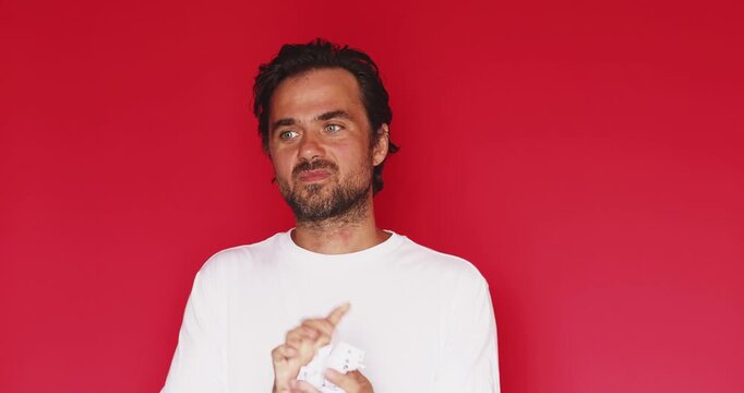Focused handsome middle aged Caucasian man reading notebook ripping out page crumpling paper and throwing it away with satisfied smile on red studio background, start fresh mistake decision concept
