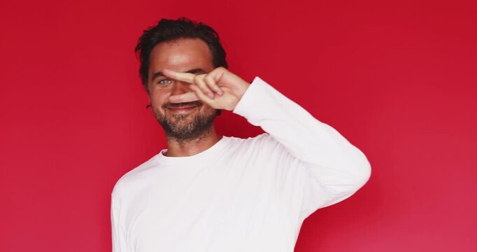 Handsome middle aged Caucasian man dancing celebrating victory showing v sign with fist pump and cheerful smile on bright red studio background, energetic happy party mood concept clip
