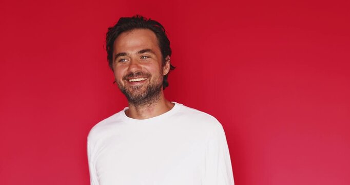 Handsome playful middle aged Caucasian man showing peace sign v gesture near eyes dancing with happy smile on bright red studio background, cheerful positive mood victory celebration concept clip