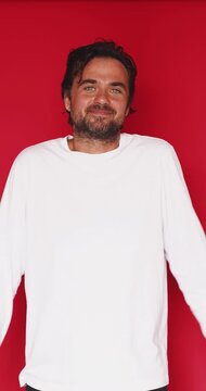 Clueless clueless middle aged Caucasian man shrugging shoulders and raising hands in innocent helpless gesture saying I do not know on bright red studio background, doubt misunderstanding concept clip