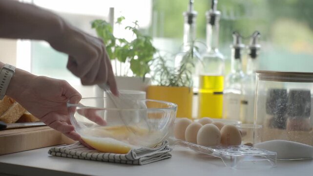 Hands whisk eggs in glass bowl with sliced bread and sugar nearby. Concept of French toast and breakfast recipe