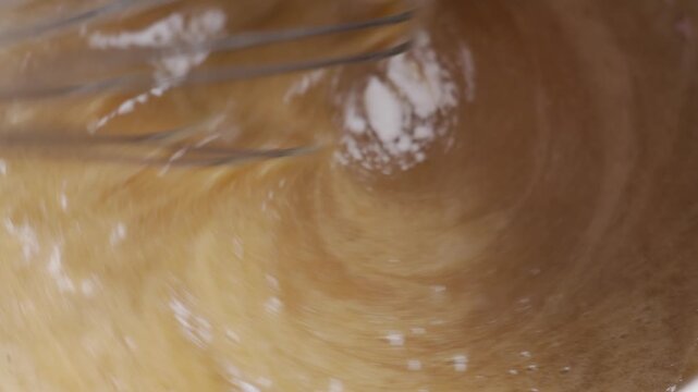 Metal whisk mixes baking soda into smooth brown cake batter. Concept of homemade baking, cake preparation and dessert recipe