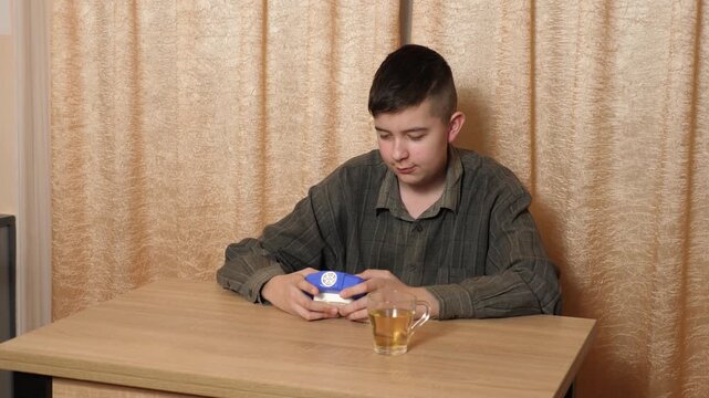Teenage boy sits at a table pressing bubbles on a Pop It fidget toy while relaxing at home with a cup of tea.
