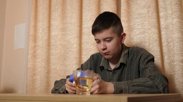 Teenage boy sits at a table pressing bubbles on a Pop It fidget toy, relieving stress and calming down while relaxing at home.