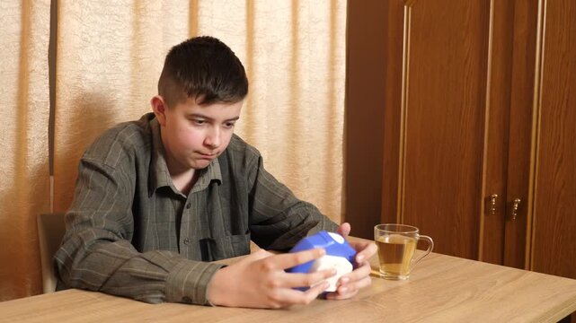 Teenage boy sits at a table pressing bubbles on a Pop It fidget toy, reducing stress and calming himself while relaxing at home.