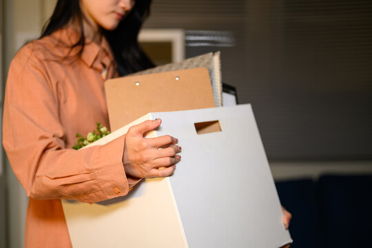 Asian businesswoman carrying personal belongings box leaving office after resignation or layoff