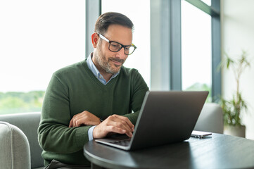 Fototapeta premium Businessman working remotely on laptop, typing during a video conference, connecting with colleagues and managing online business tasks from a casual office environment