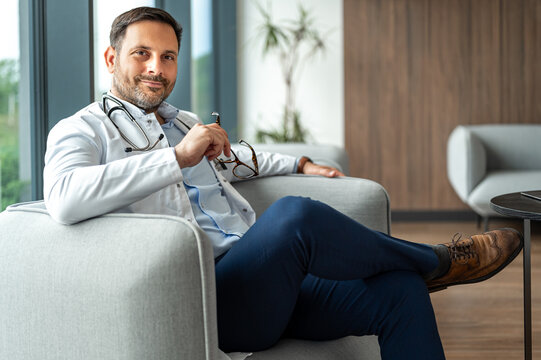 Doctor sitting relaxed in a stylish professional environment, confidently holding glasses, symbolizing expertise, trust, and dedicated healthcare services