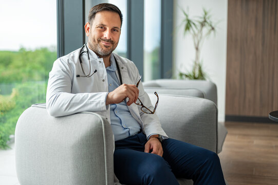 Experienced male physician in a medical uniform, holding eyeglasses and smiling, representing healthcare expertise and professional medical service