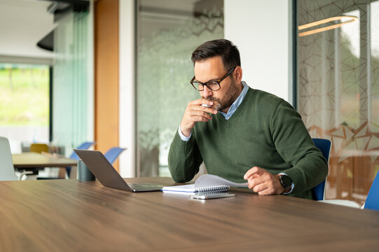 Professional male entrepreneur concentrating on work tasks at a meeting room table, thinking critically about financial analysis and corporate development