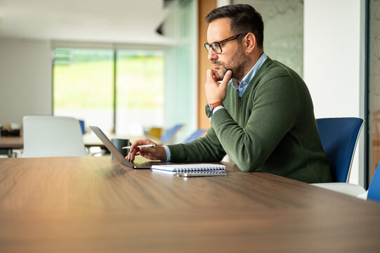 Businessman concentrating on his work at a table, processing information and making strategic decisions for a professional venture in a contemporary office setting