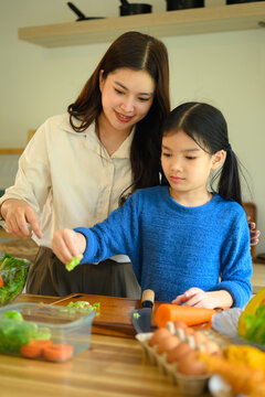 Mother and Daughter Cooking Together in Kitchen, Chopping Fresh Vegetables on Wooden Cutting Board