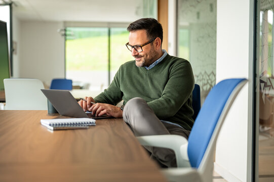 Businessman smiling while working on a laptop, concentrating on a project, demonstrating productivity and a professional attitude in a contemporary office workspace