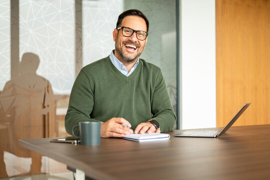 Businessman laughing while working at a modern desk, capturing joy, achievement, and positive work culture in a dynamic corporate setting, reflecting a happy and thriving professional