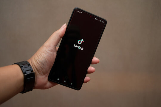 Riau, July 26, 2026, Close-up view of a hand holding a smartphone showing the TikTok app splash screen against a neutral backdrop. Great for social media, marketing, and tech topics.