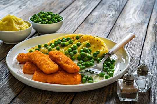 Fried fish sticks with mashed potatoes and green peas on wooden table