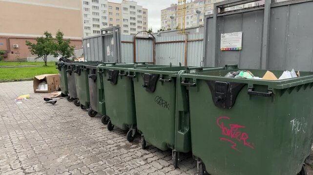 Green trash containers are lined up beside a city sidewalk, efficient waste collection, urban infrastructure, eco awareness, sustainable living.