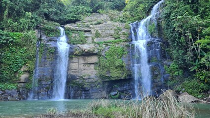 Scenic double waterfall cascading down rocky cliffs into a pristine river surrounded by lush green tropical jungle foliage © MdAbu