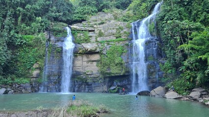 Beautiful twin waterfall cascading into a clear natural emerald pool surrounded by lush tropical green jungle forest rocks landscape © MdAbu