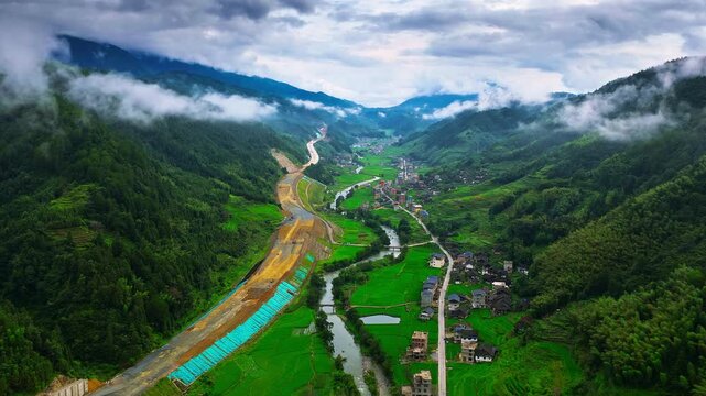High angle view of road construction site in green mountain valley near Guilin, Guangxi, China. Highway development project cuts through rural countryside landscape with mist.