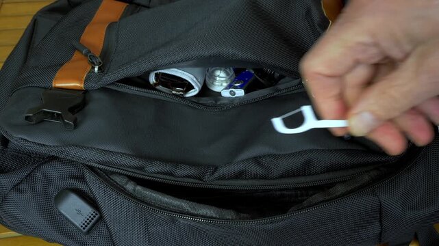 Closeup of a man&rsquo;s hand packing personal items into the zip pockets of a soft travel bag, finishing off with a toothbrush.