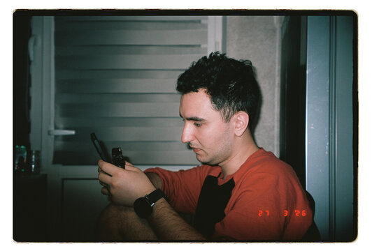 A man scrolls his phone in dim indoor light 