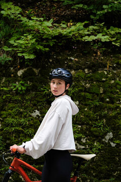 Young female cyclist walking with her bicycle along a green forest 