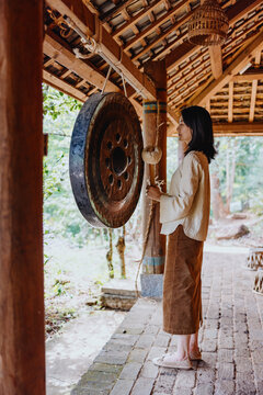 Woman Striking Traditional Gong in Wooden Pavilion