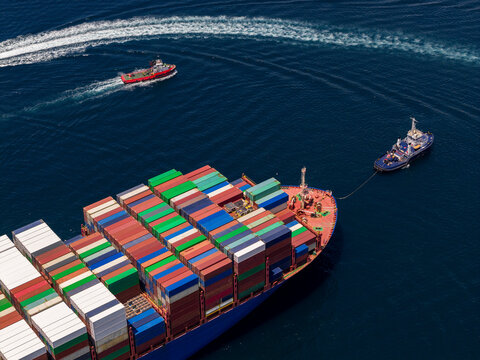 Container ship navigating port waters with tugboat assistance