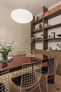 Dining room with oxblood table, wire chairs and walnut bookcase