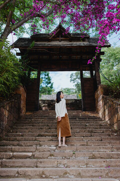 Woman Standing on Stone Steps Beneath Traditional Wooden Gate