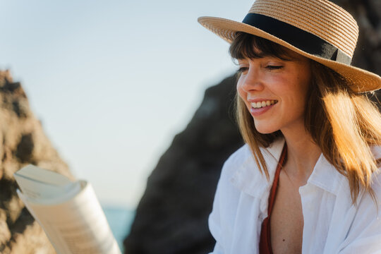 Pretty woman reads a book on the rocky beach