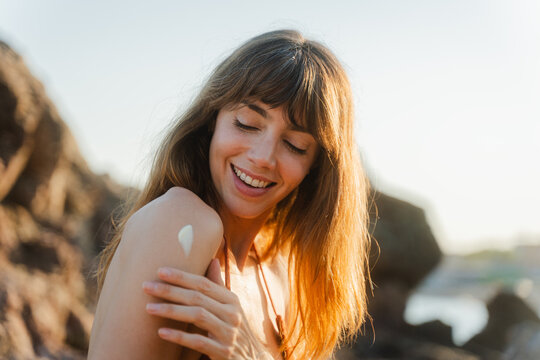 Smiling woman applies sun lotion on her shoulder