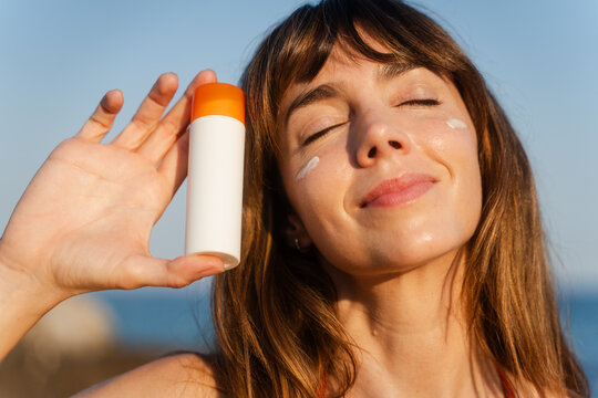 Woman beams with joy, holding a tube of sunscreen