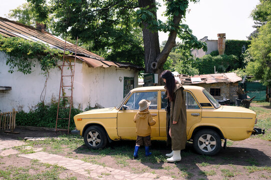 Mother and son standing by an old yellow car in a park